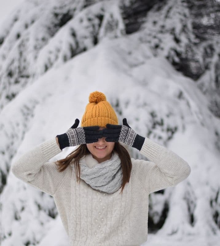 A mustard-yellow knitted beanie pulled down, cream sweater, snow behind.