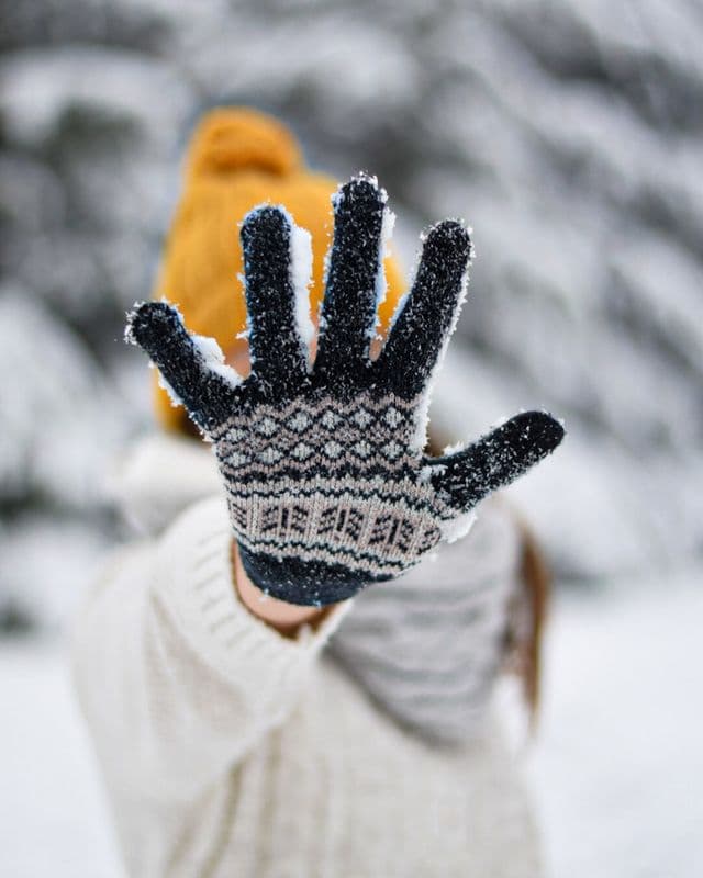 A patterned knitted glove held up against falling snow.